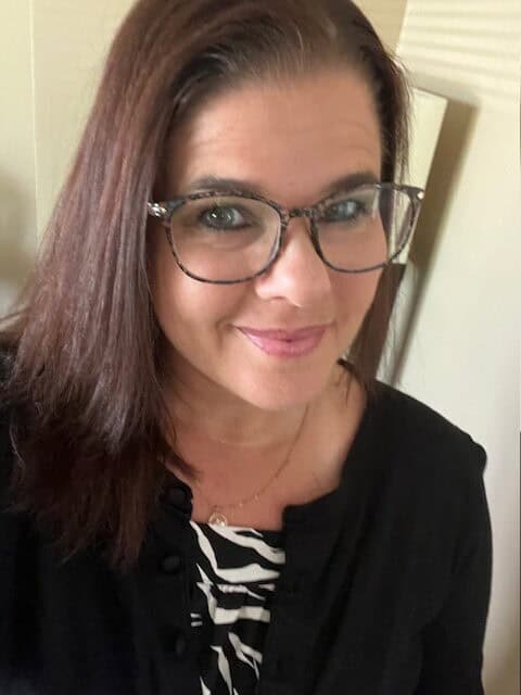 Portrait of a JFK Catholic School teacher with glasses smiling.