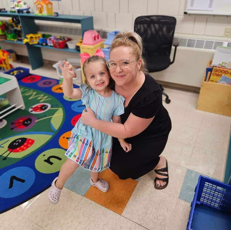 Bristy Potter hugging a young girl in a classroom setting.