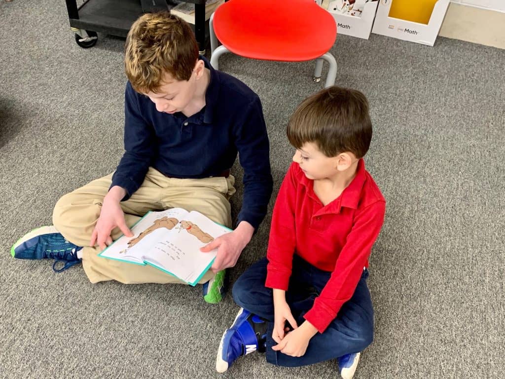 Two boys sitting on the carpet reading a book in JFK Catholic School classroom.