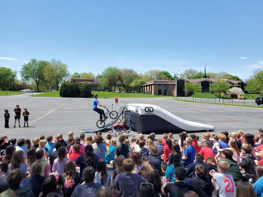 Students watching a BMX stunt at JFK Catholic School outdoor event.