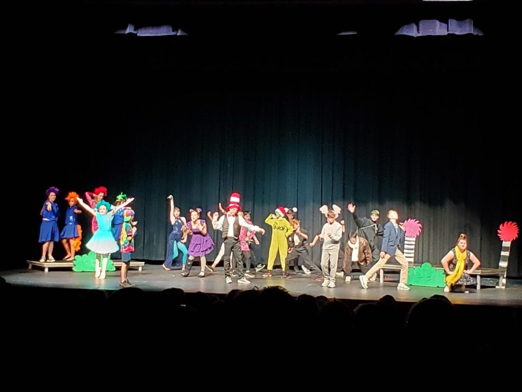 Students performing a school play on stage with colorful costumes.