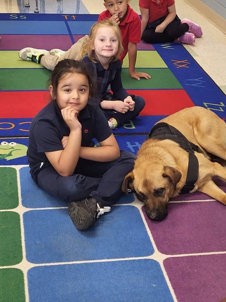 Students at JFK Catholic School with therapy dog in classroom setting.