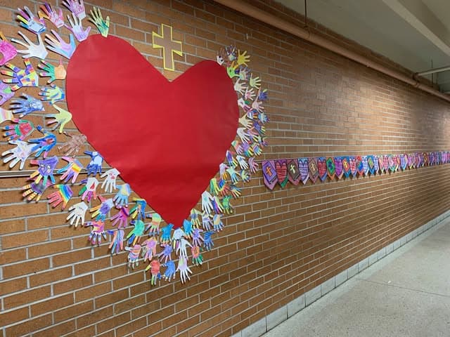 Colorful heart and hand mural display at JFK Catholic School hallway.
