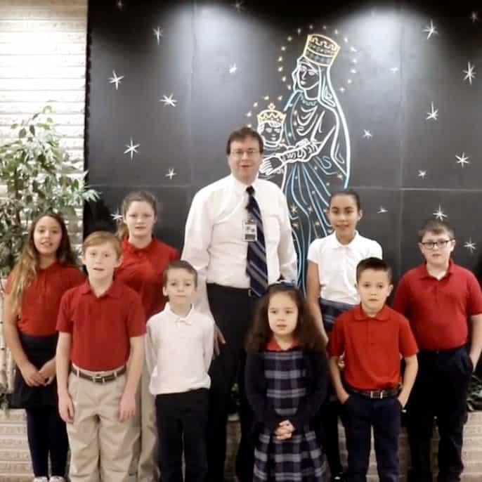 Principal standing with children by picture of Mary.