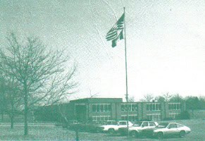 Historic JFK Catholic School building with American flag and parking lot.