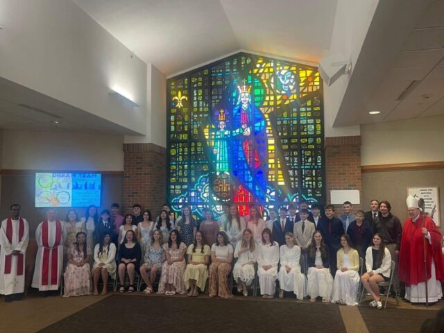 A vibrant stained glass window featuring a religious figure with students and faculty in front.