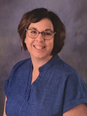 Preschool teacher Melissa Zeimet smiling, wearing glasses and a blue shirt at JFK Catholic School.