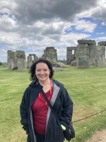 Woman smiling at Stonehenge with cloudy sky background.