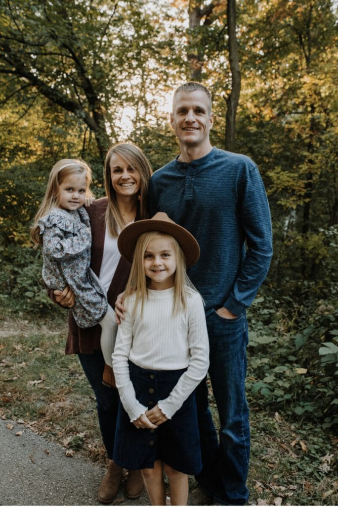Family of four smiling outdoors in autumn at JFK Catholic School.