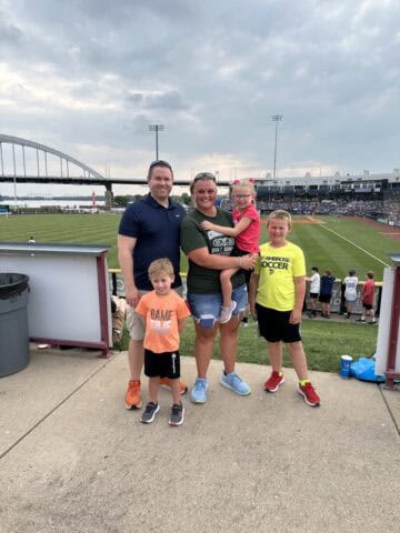 Family at JFK Catholic School soccer game with children and coach on field.