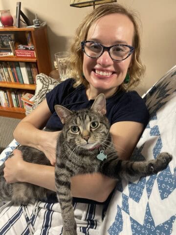 Smiling girl holding a tabby cat in a cozy home setting, promoting preschool education at JFK Cathol.